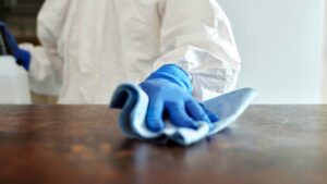 gloved hand wipes down a surface, with spray bottle and rag.